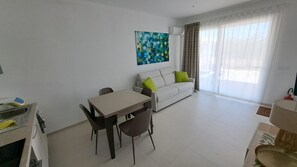 A modern living room with a dining area, a sofa with cushions, a painting on the wall, and a large window with curtains. - Beachfront villa with a garden and private parking on the property. (Avola)