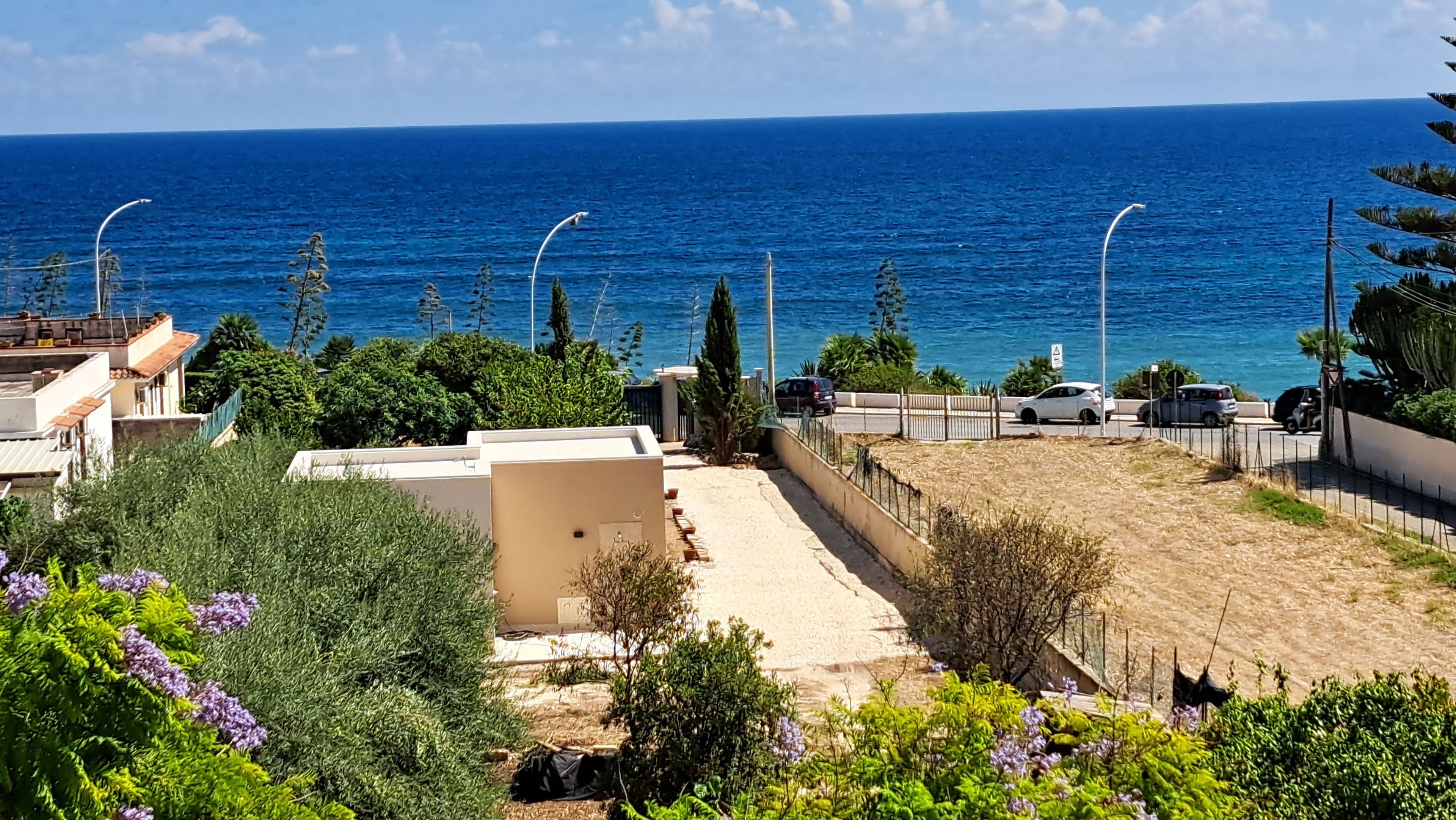 Un quartier résidentiel offrant une vue sur la mer, avec une allée pavée et une cour clôturée agrémentée de quelques plantes.