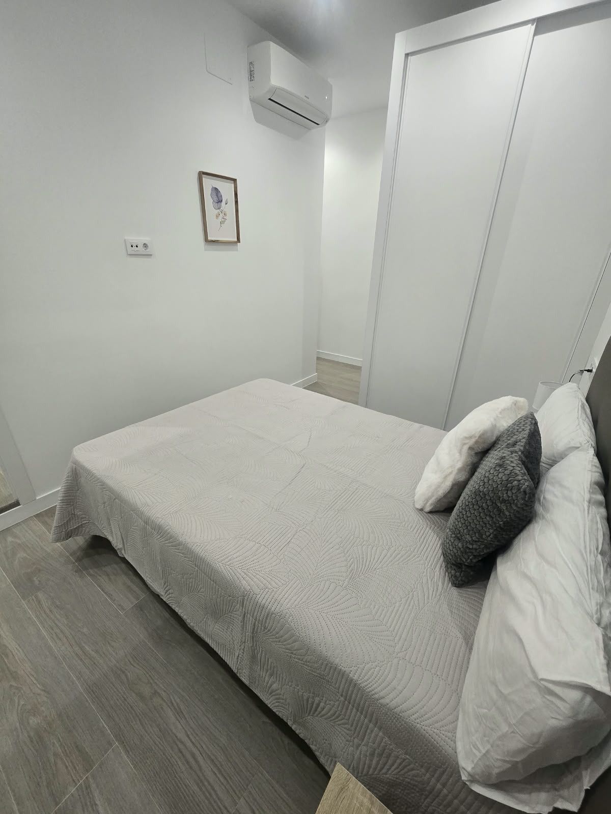 Ein Schlafzimmer mit einem Bett, einem Nachttisch, einer Wand-Klimaanlage und einer Tür.