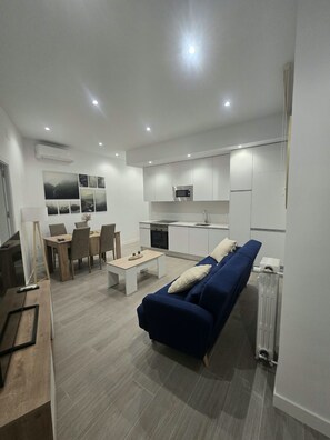 A modern living space with a dining area, kitchenette, and a blue sofa. - (ALC124) 3 bedroom apartment in Goya (Madrid)