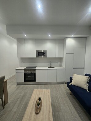 A modern kitchen with built-in appliances, a dining area with a wooden table, and a blue sofa. - (ALC124) 3 bedroom apartment in Goya (Madrid)