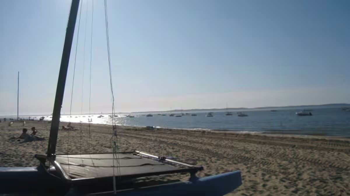 A beach with a sailboat in the foreground and several boats in the water.