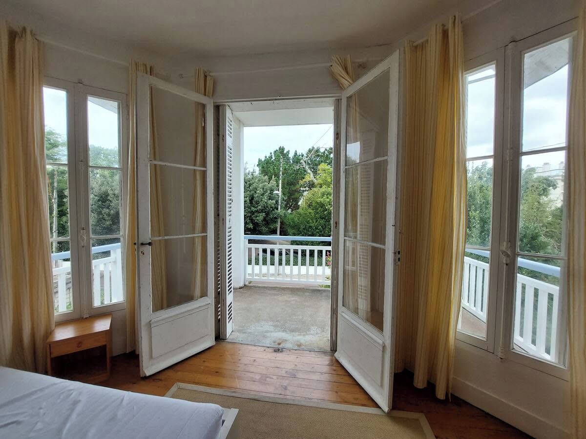 A bedroom with a large window, a wooden bench, and a view of a balcony.