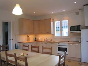 A compact kitchen with wooden cabinets, a dining table with chairs, a microwave, and a refrigerator. - Large family villa 50m from the beach (Arcachon)