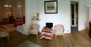A room with a wooden floor, a table with chairs, a television, a framed picture on the wall, and a doorway leading to another room. - Large family villa 50m from the beach (Arcachon)