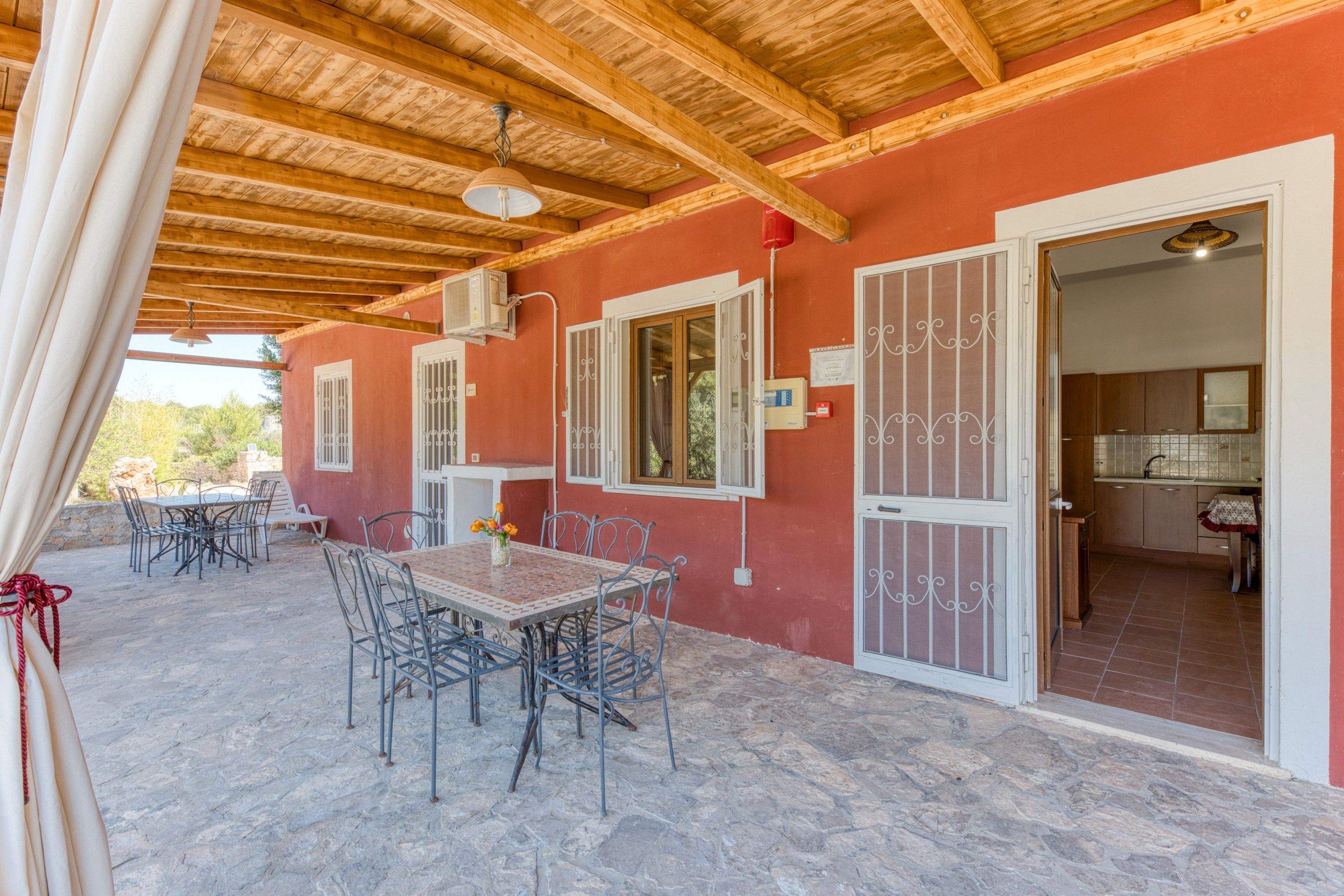 Un portico esterno coperto, con pavimento in pietra, mobili in metallo e soffitto in legno.
