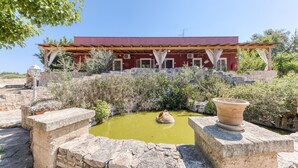 A building with a red facade, a stone wall, and a small water feature with a pot. - Apartment 'Le Colonie - Bilocale 2' with Private Terrace, Shared Garden and Air Conditioning (Presicce)