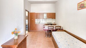 A compact room with a bed, a small table with a vase of flowers, a dining table with chairs, and a kitchen area with cabinets and a sink. - Apartment 'Le Colonie - Bilocale 2' with Private Terrace, Shared Garden and Air Conditioning (Presicce)