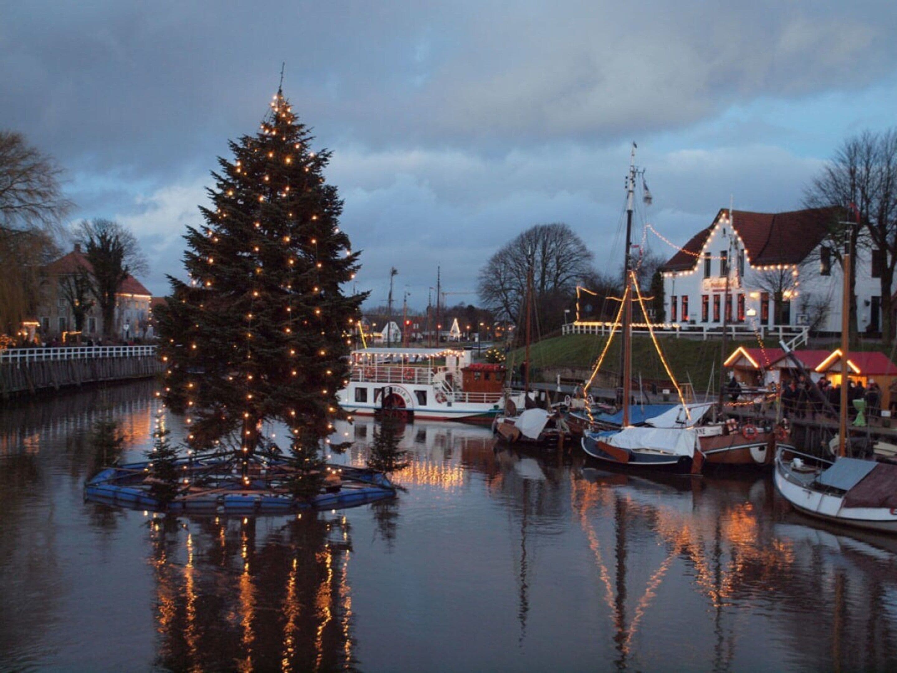 A waterfront scene with a decorated Christmas tree, boats, and buildings along the shore.