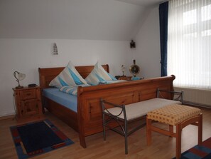 A bedroom with a wooden bed, bedside tables, a bench, and a window with curtains. - Holiday Apartment With 2 Bedrooms (Wittmund)