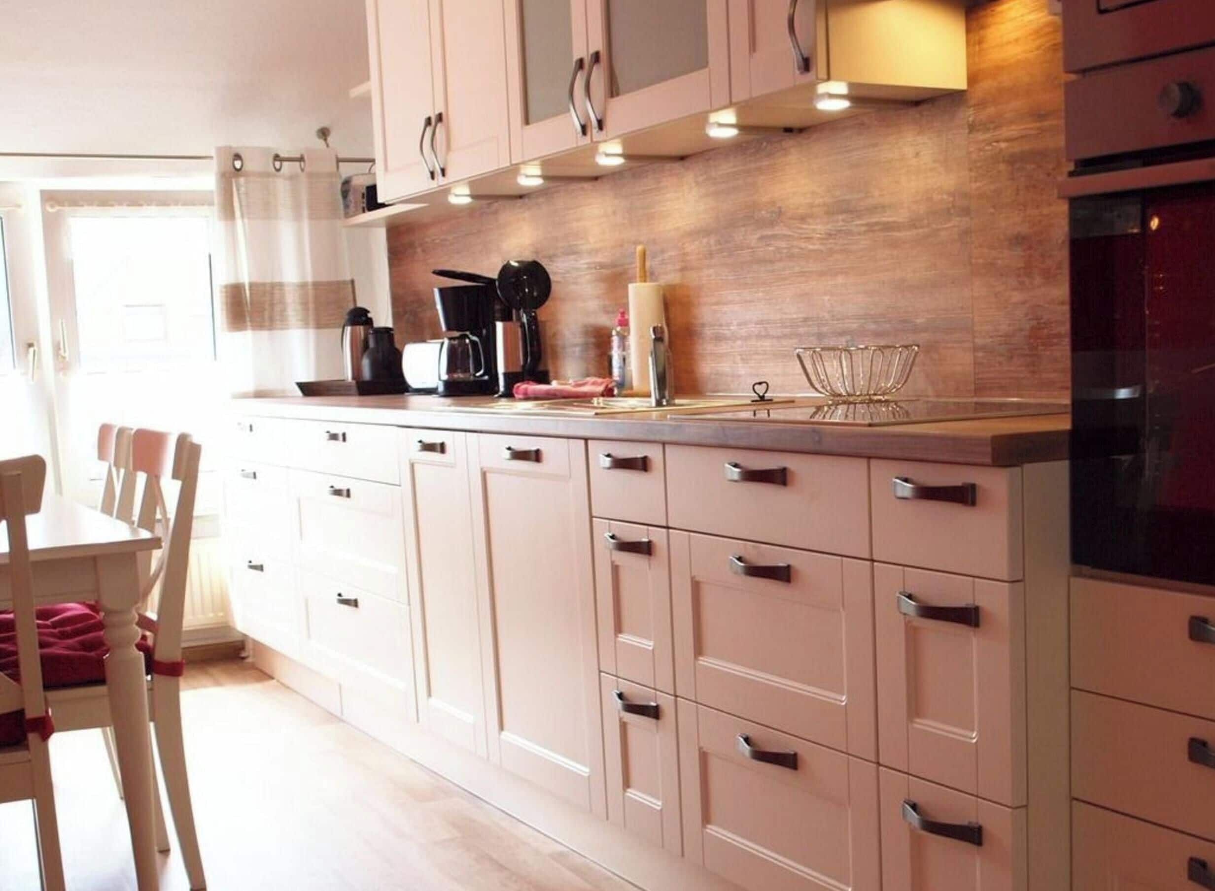 Una cocina moderna con armarios de colores claros, encimera de madera y una zona de comedor con mesa y sillas.