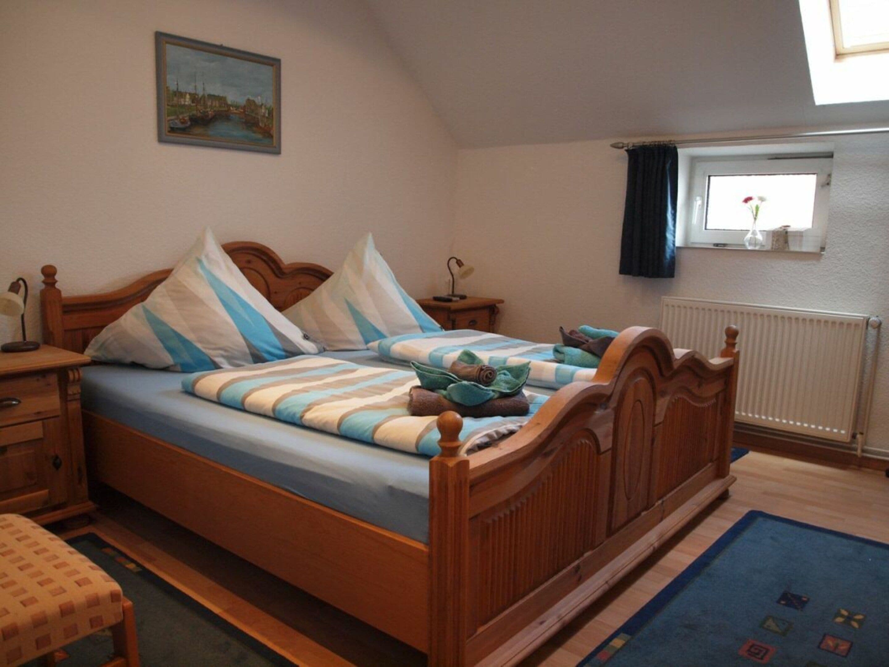 A bedroom with a wooden bed, a nightstand, a desk, a chair, a window with curtains, and a painting on the wall.