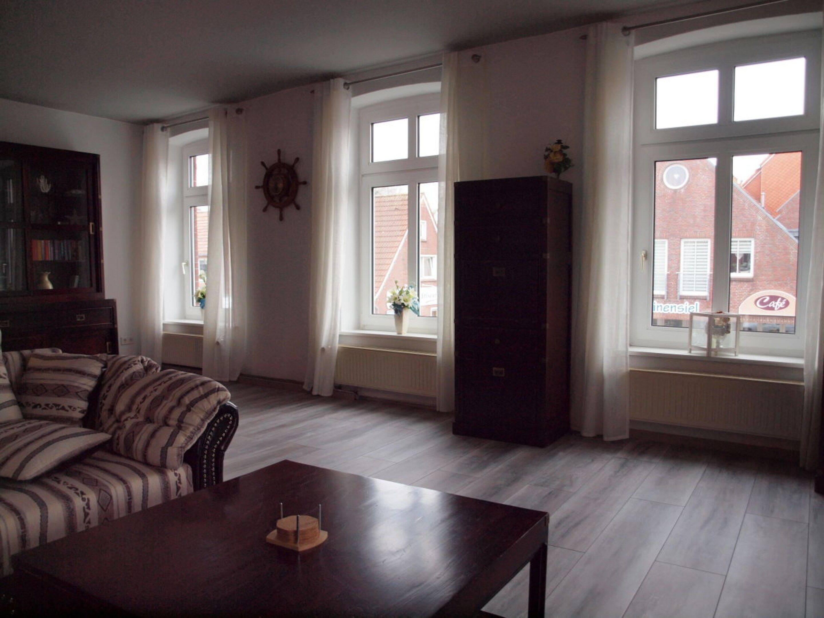 A living room with a sofa, a wooden coffee table, and a large window with curtains.