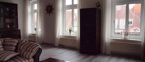 Una sala de estar con un sofá, una mesa de centro de madera y un amplio ventanal con cortinas.