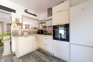 A modern kitchen with white cabinetry, a black oven, and a countertop with various items. - Villa 'La Garrigue en Provence' with private pool, air conditioning, 3,000 m² garden, 4 guests (Taradeau)