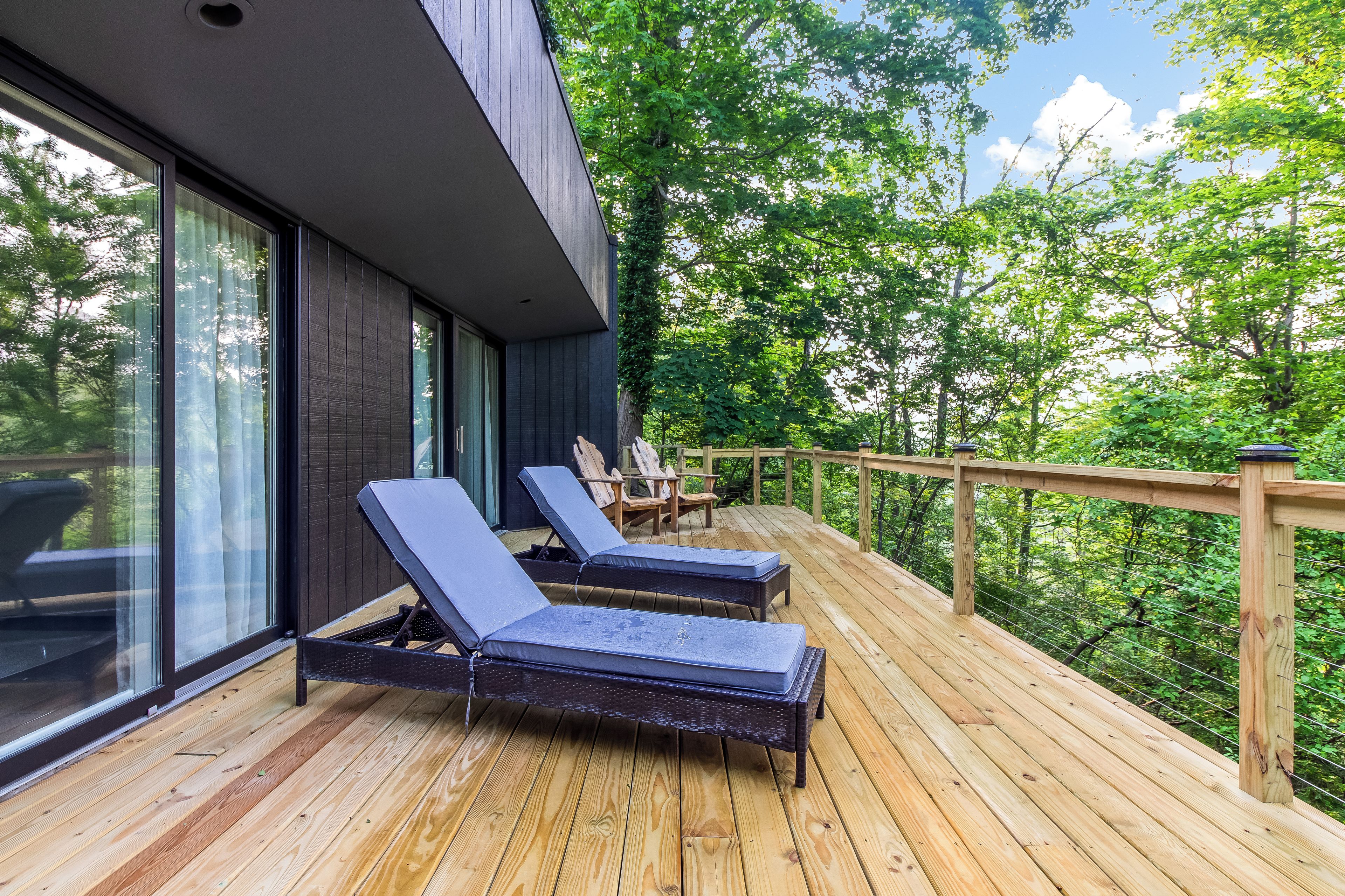 A wooden deck with lounge chairs, a railing, and a view of trees.