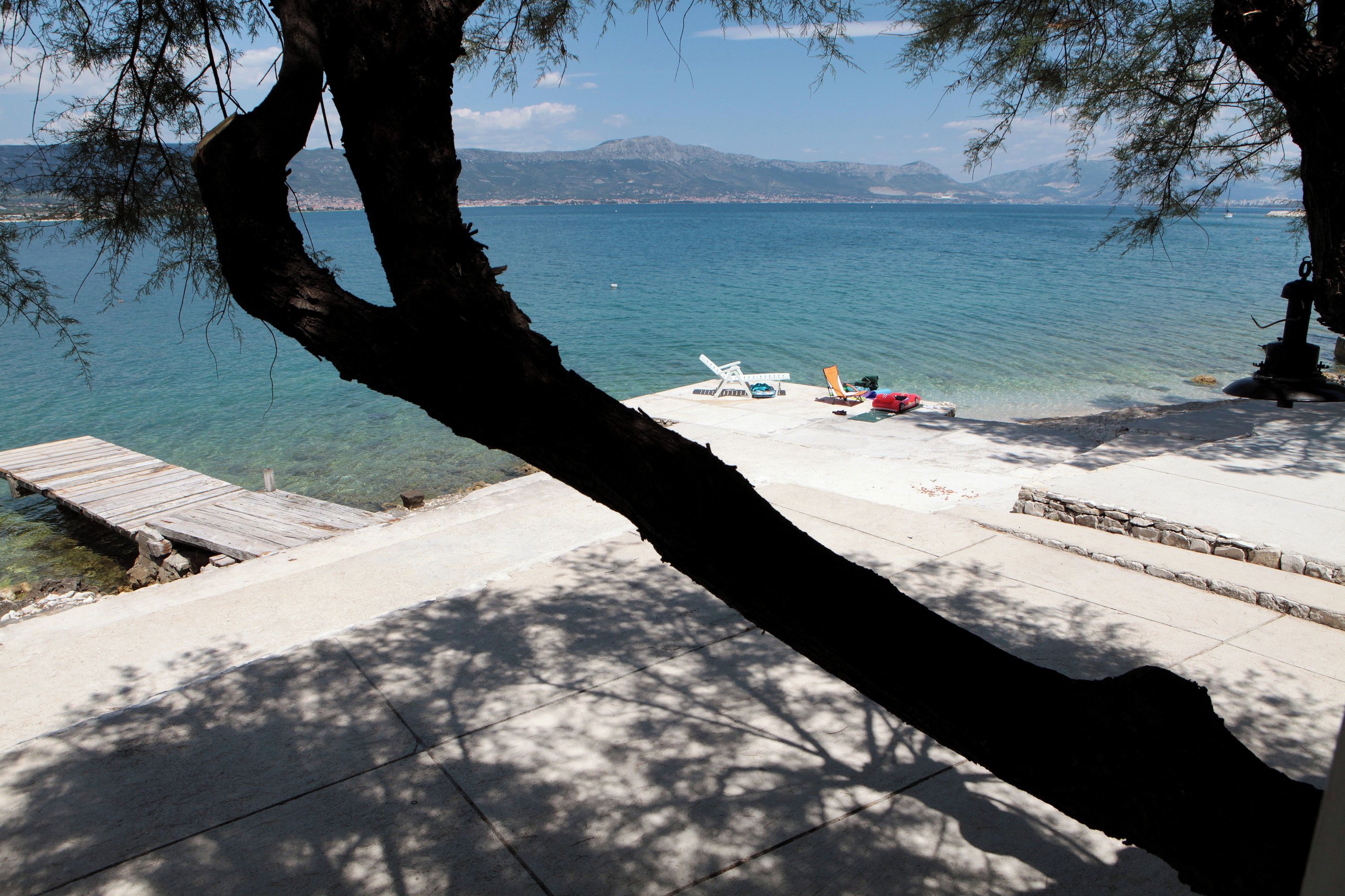 A clear view of a lake with a wooden dock leading to a beach area with lounge chairs and a small statue.