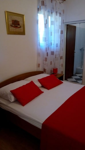 Een hotelkamer met een bed, rode kussens, een ingelijst foto op de muur en een badkamer zichtbaar door een geopende deur.