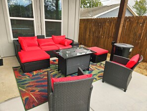 Eine Terrasse mit Korbmöbeln, einem Glastisch und einem farbenfrohen Teppich.
