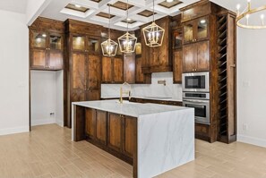 A kitchen with wooden cabinets, a marble island, and modern appliances. - Villa Del Gotti A Luxury Stockyards Experience (Fort Worth)