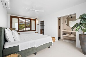 A modern bedroom with a bed, a ceiling fan, a window with blinds, a bathroom with a sink and mirror, and a potted plant. - NEW Oceanview villa, private gym and infinity pool! (Kralendijk)