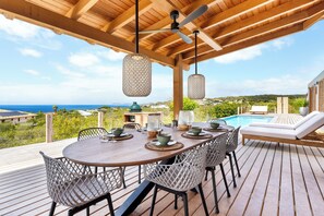 A wooden deck with a table set for dining, overlooking a swimming pool and the sea. - NEW Oceanview villa, private gym and infinity pool! (Kralendijk)