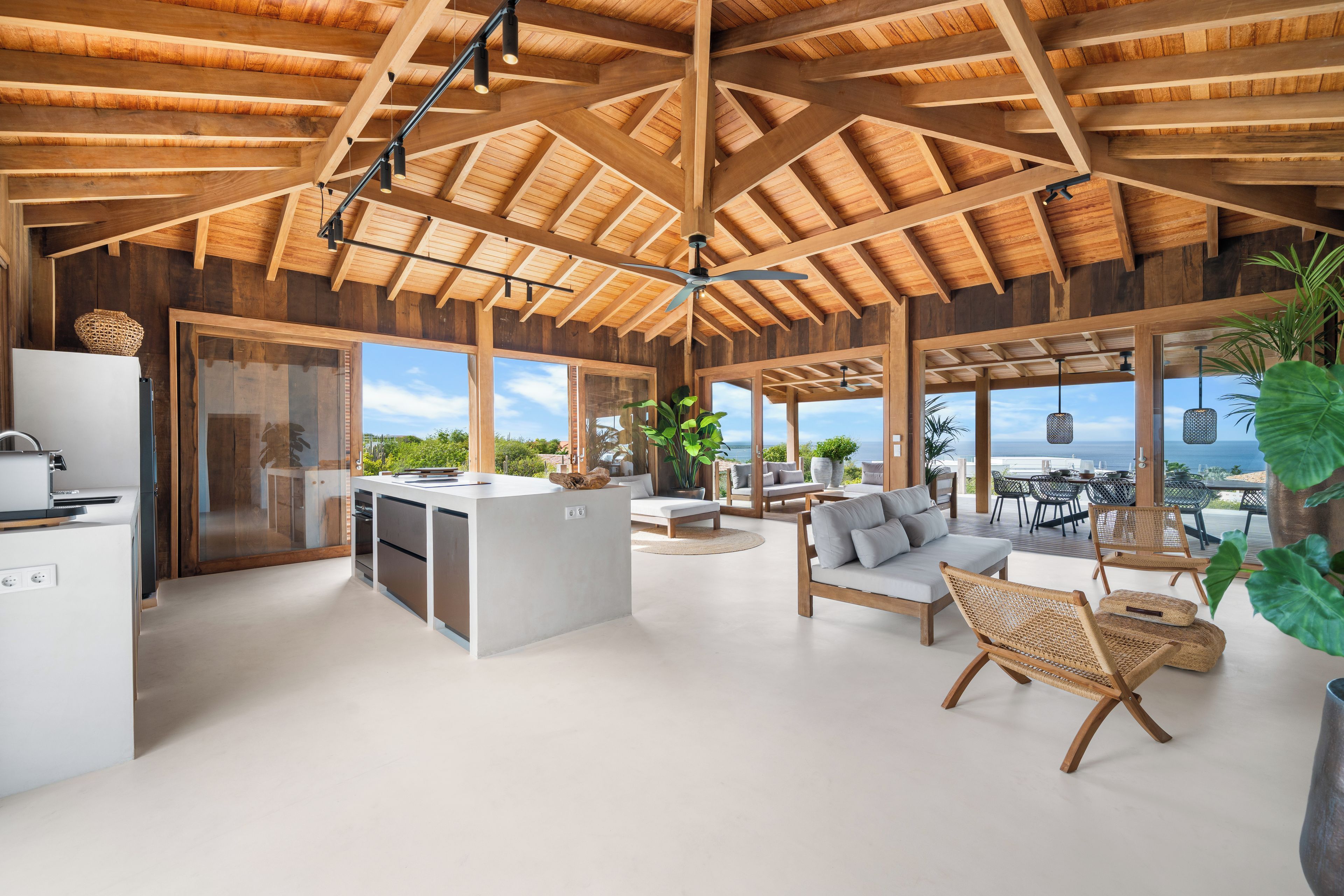 A spacious living area with a high wooden ceiling, a central island, and a view of the ocean.