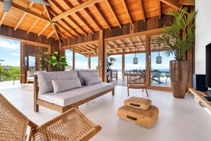 A spacious living area with a wooden ceiling, a sofa, wicker chairs, and a large plant. - NEW Oceanview villa, private gym and infinity pool! (Kralendijk)