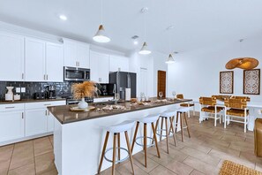 A modern kitchen with white cabinetry, stainless steel appliances, and a central island with bar stools. - Disney Area Villa w Private Pool & Resort Access (Davenport)