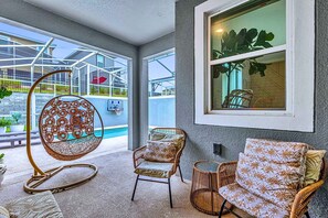 A modern outdoor seating area with wicker chairs and a hanging chair, a pool, and a view of a building with a glass facade. - Disney Area Villa w Private Pool & Resort Access (Davenport)