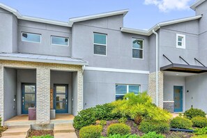 A modern multi-story residential building with a covered front porch, stone columns, and a well-maintained garden. - Disney Area Villa w Private Pool & Resort Access (Davenport)