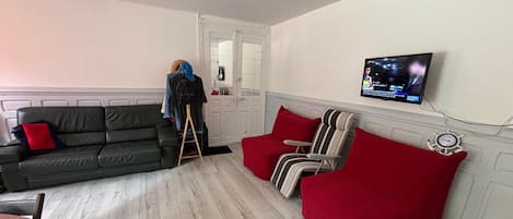 A living room with a sofa, a red armchair, a television mounted on the wall, and a wooden floor.