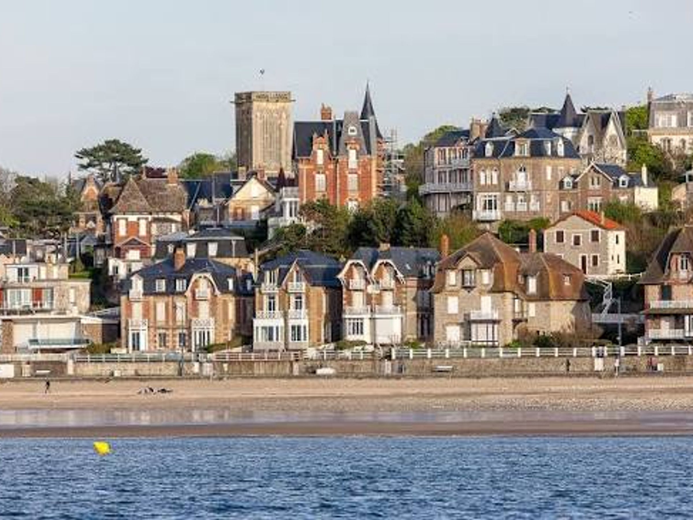 A coastal town with historic buildings, a beach, and a clear sky.