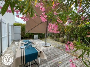 An outdoor dining area with a table set for two, surrounded by greenery and pink flowers. - Family cottage on Île d'Yeu - 6 guests (L'Île-d'Yeu)