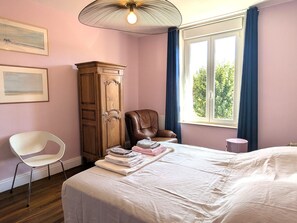 Quarto com cama, uma cadeira, guarda-roupa e janela com cortinas.
