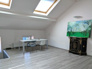 Ein Zimmer mit Dachfenster, Schreibtisch, Stuhl, Heizkörper und einem Bild an der Wand.
