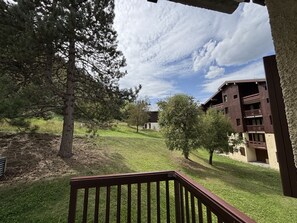 Ein Gebäude mit einer Holzterrasse im Vordergrund, einer Rasenfläche mit Bäumen und einem wolkenlosen Himmel.