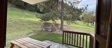 Una mesa de madera en un patio de piedra con vistas a una colina cubierta de hierba y árboles.