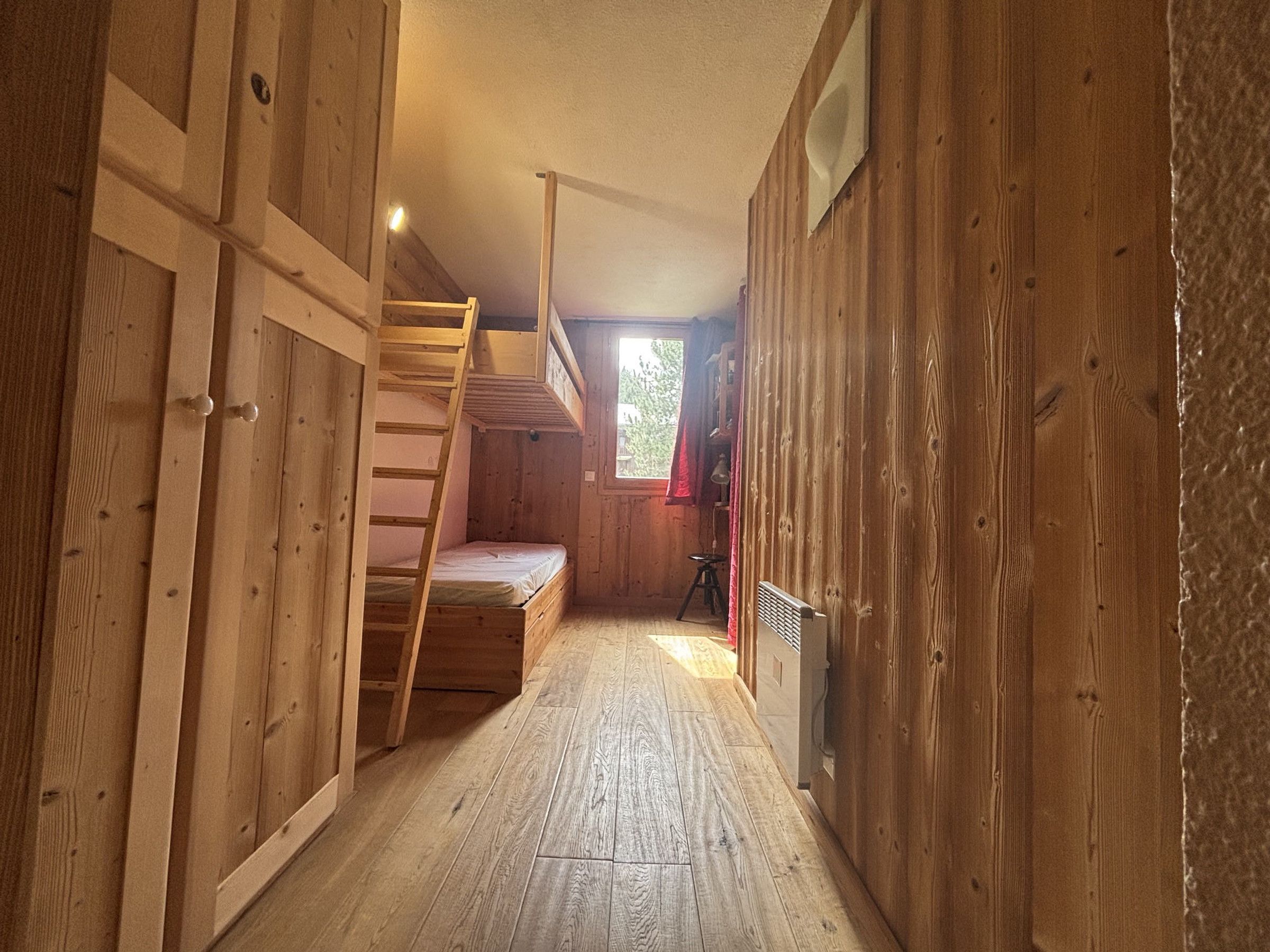 Ein schmales Zimmer mit Holzwänden, einem Etagenbett, einer Stehleiter und einer Heizung.