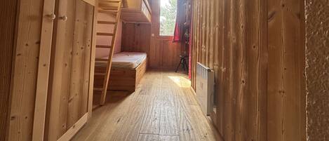 A narrow wooden room with a bunk bed, a ladder, and a radiator.