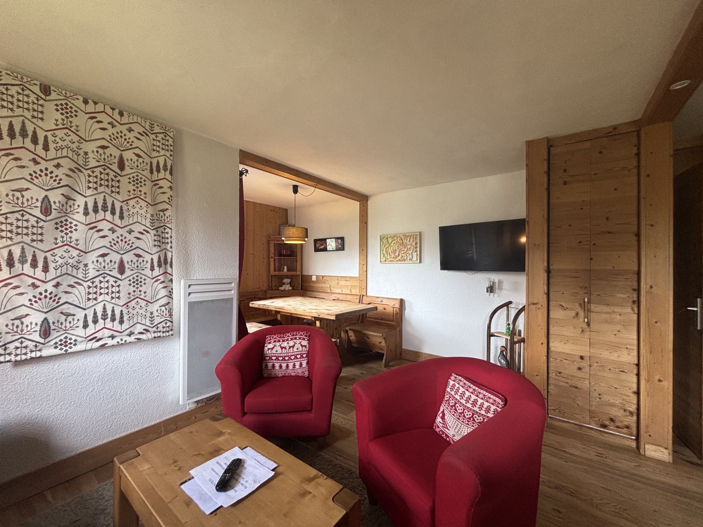 A room with two red armchairs, a wooden table, a television, and a patterned wall.