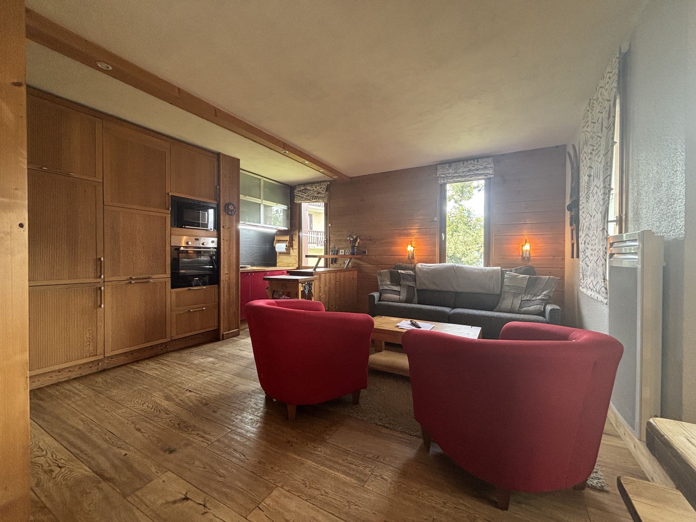 Un espace de vie compact comprenant un coin cuisine, un canapé et deux fauteuils.