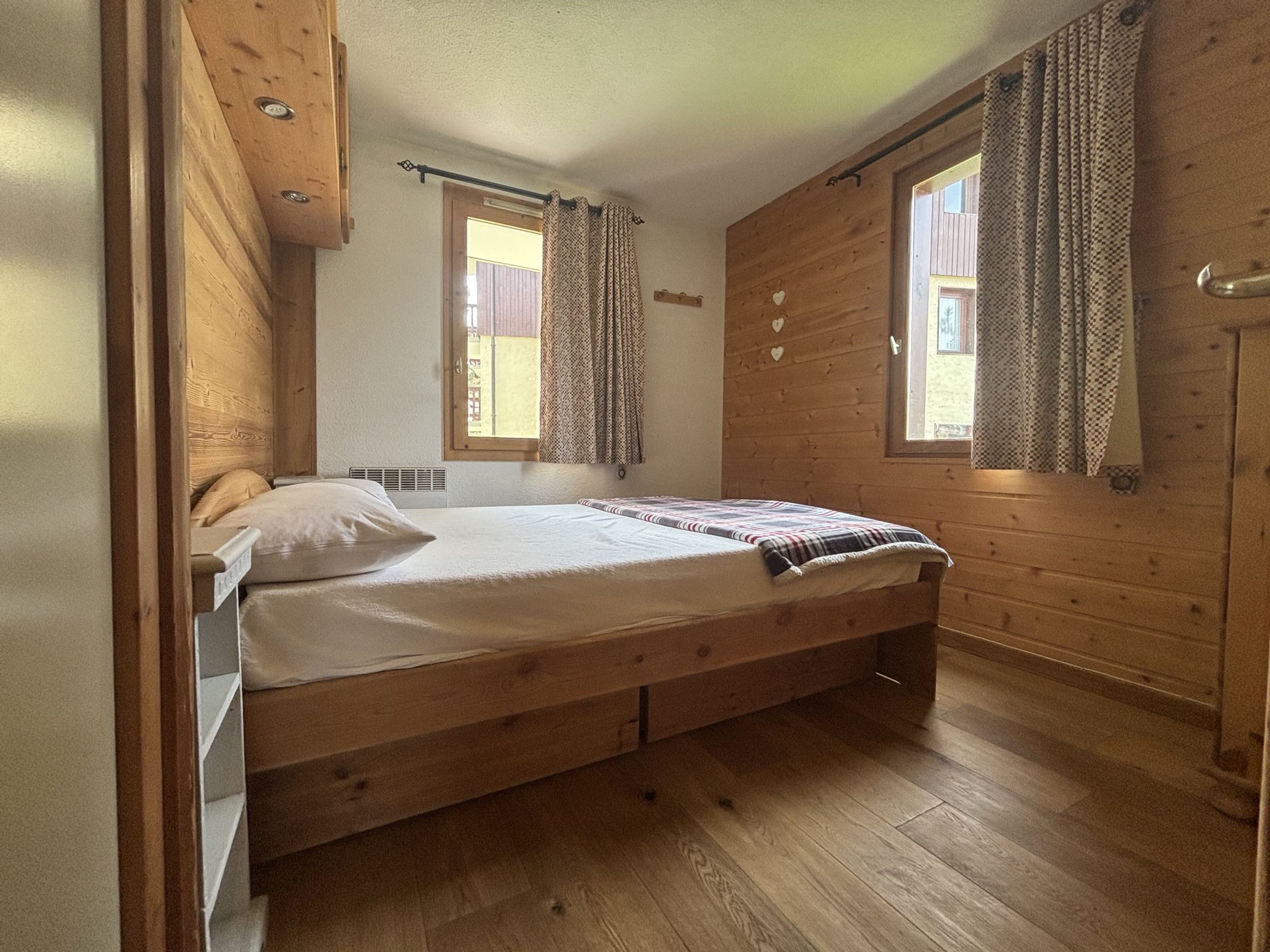Ein Schlafzimmer mit Holzbalken, einem Bett, zwei Vorhängen und einem Heizkörper.