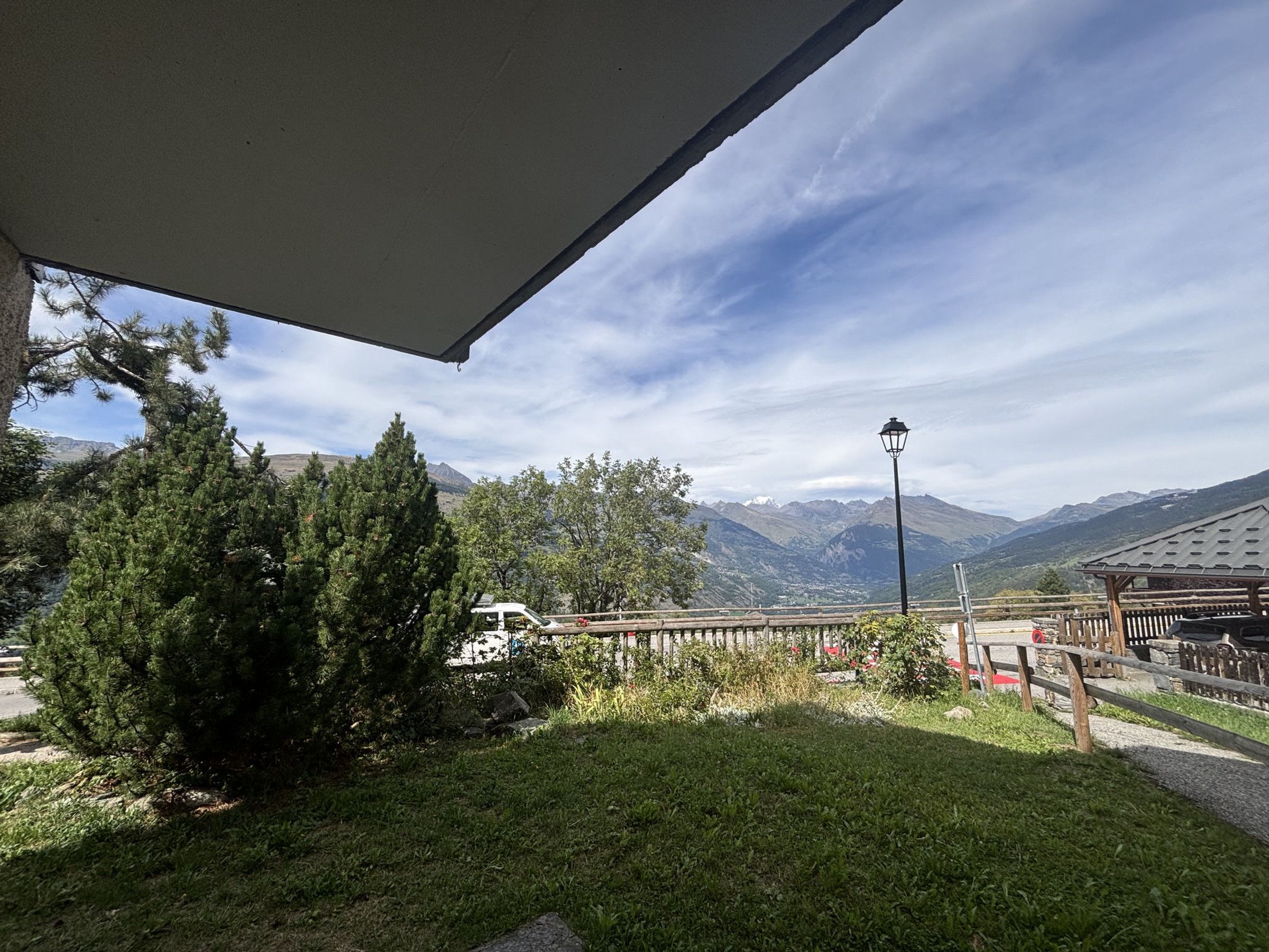 A covered outdoor area with a view of mountains, a wooden fence, and a street lamp.