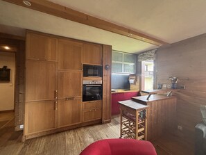 A compact kitchen with wooden cabinetry, a built-in oven, and a small countertop. - Montchavin Apartment, Mont Blanc View - 7 guests (La Plagne Montchavin Les Coches)