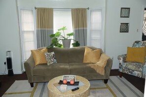 Ein Wohnzimmer mit einer Couch, Sesseln, einem Couchtisch mit Zeitschriften und einer Fernbedienung, einer Topfpflanze und einem Streifenmuster-Teppich.
