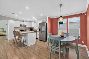 A modern kitchen with white cabinetry, stainless steel appliances, and a dining area with a round table and chairs.