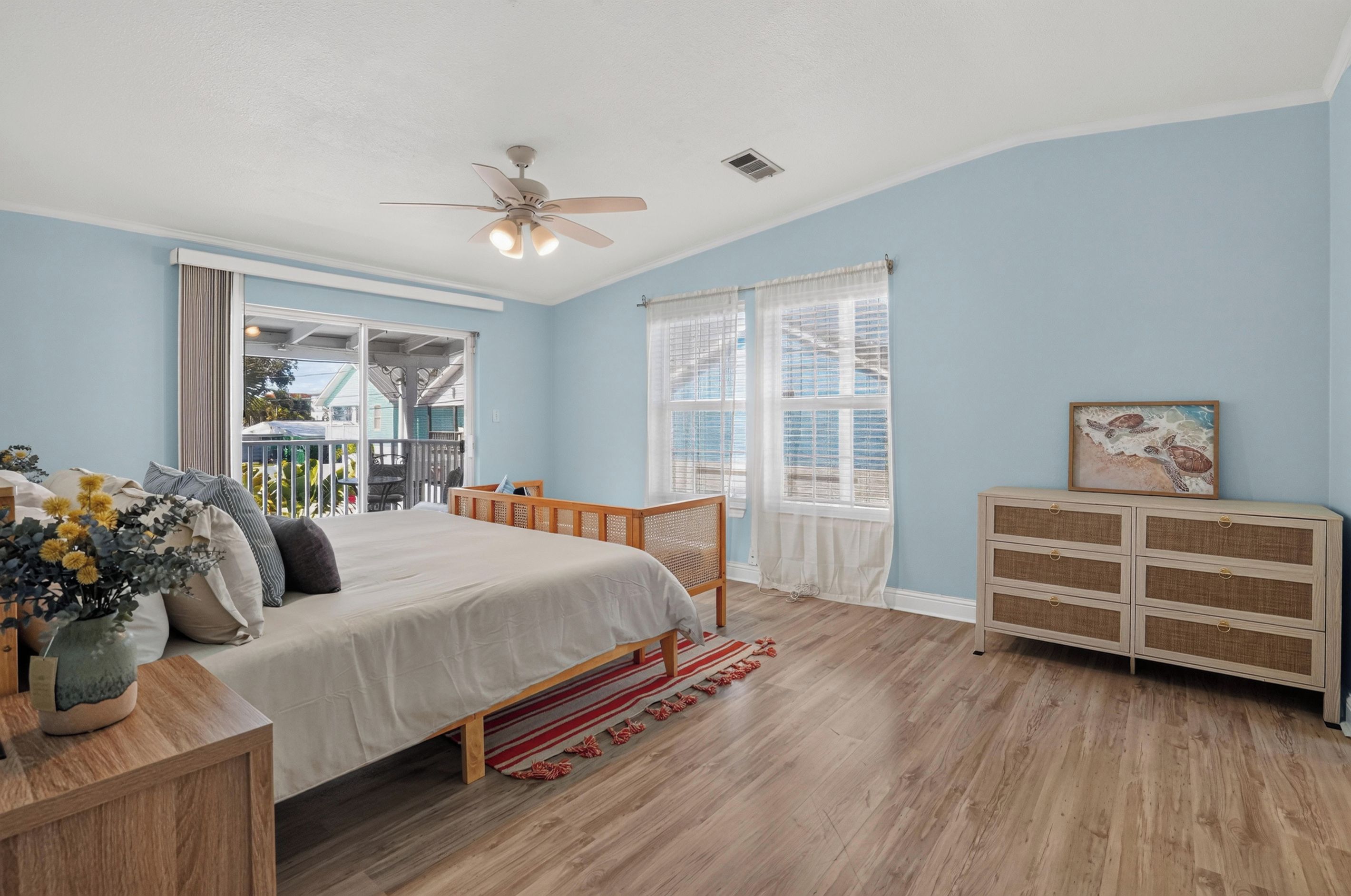 Une chambre à coucher avec un lit, une commode, un ventilateur de plafond et une fenêtre avec des rideaux.
