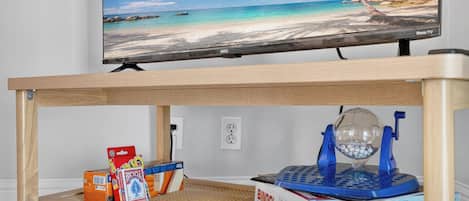 A television displaying a beach scene, a wooden table with a BINGO set, and a blue and white object on the table.