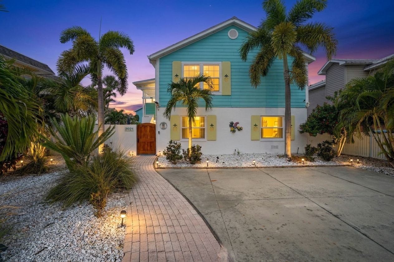 A two-story house with a front porch, palm trees, and a driveway.